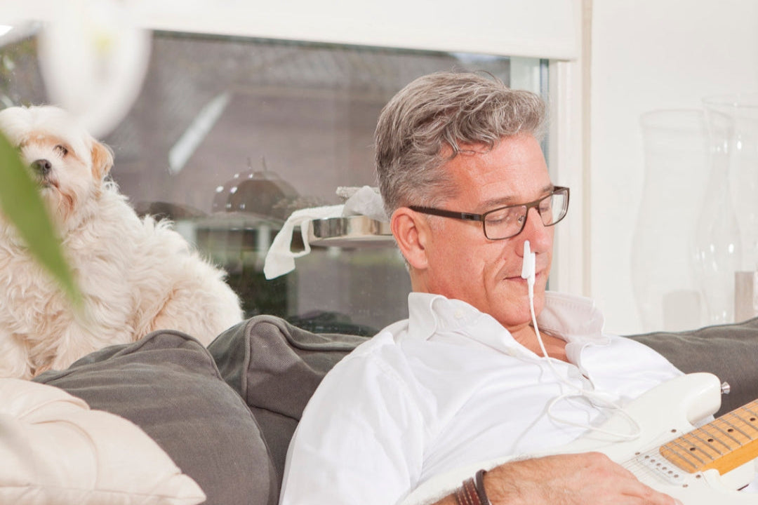 Man met rood licht therapie laser in de neus met gitaar vast en hond op de achtergrond lichttherapie voor thuis